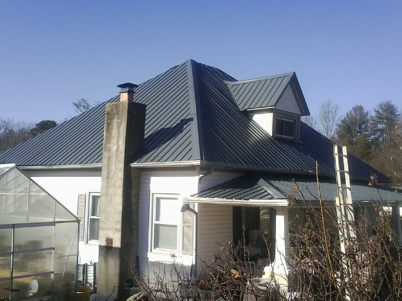 Dark blue standing seam metal roof on a white farmhouse with dormer — Slate & Tile Roof Repair by Roofing Brothers in Harpersville