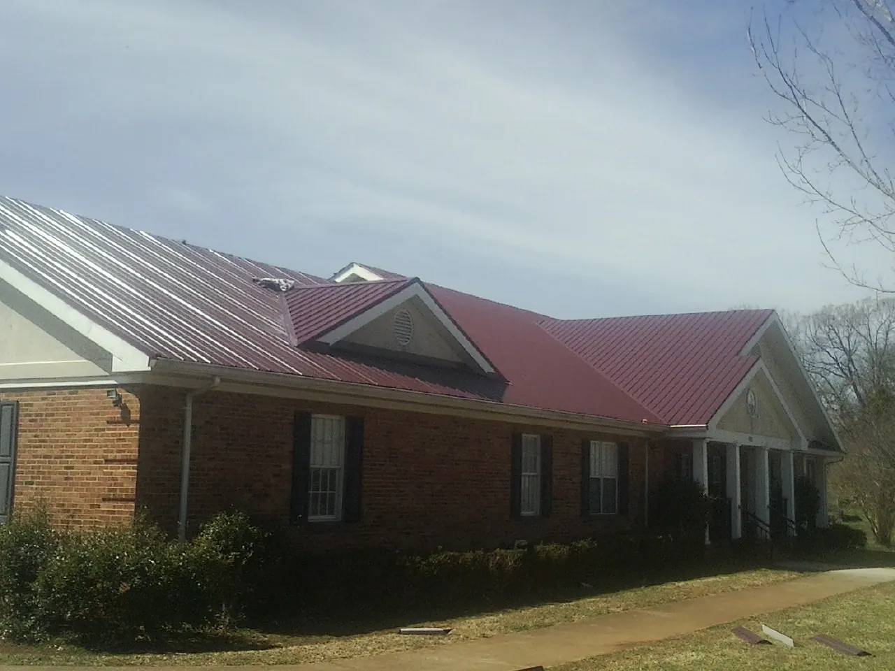 Red metal roof with gabled entries on a long brick building, from a Hail Damage Roof Repair job in Harpersville