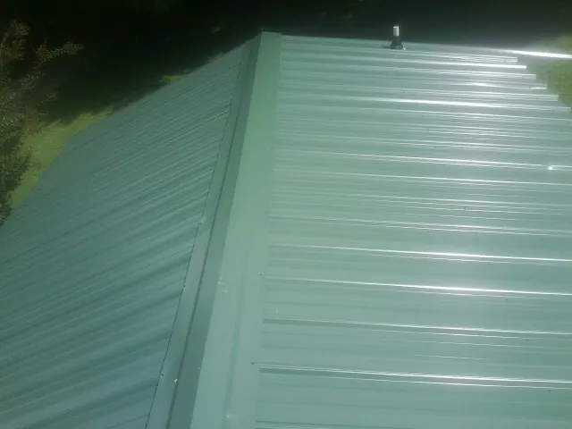 New green metal panels meeting at the ridge of a roof — Flat Roof Repair work by our crew in Harpersville