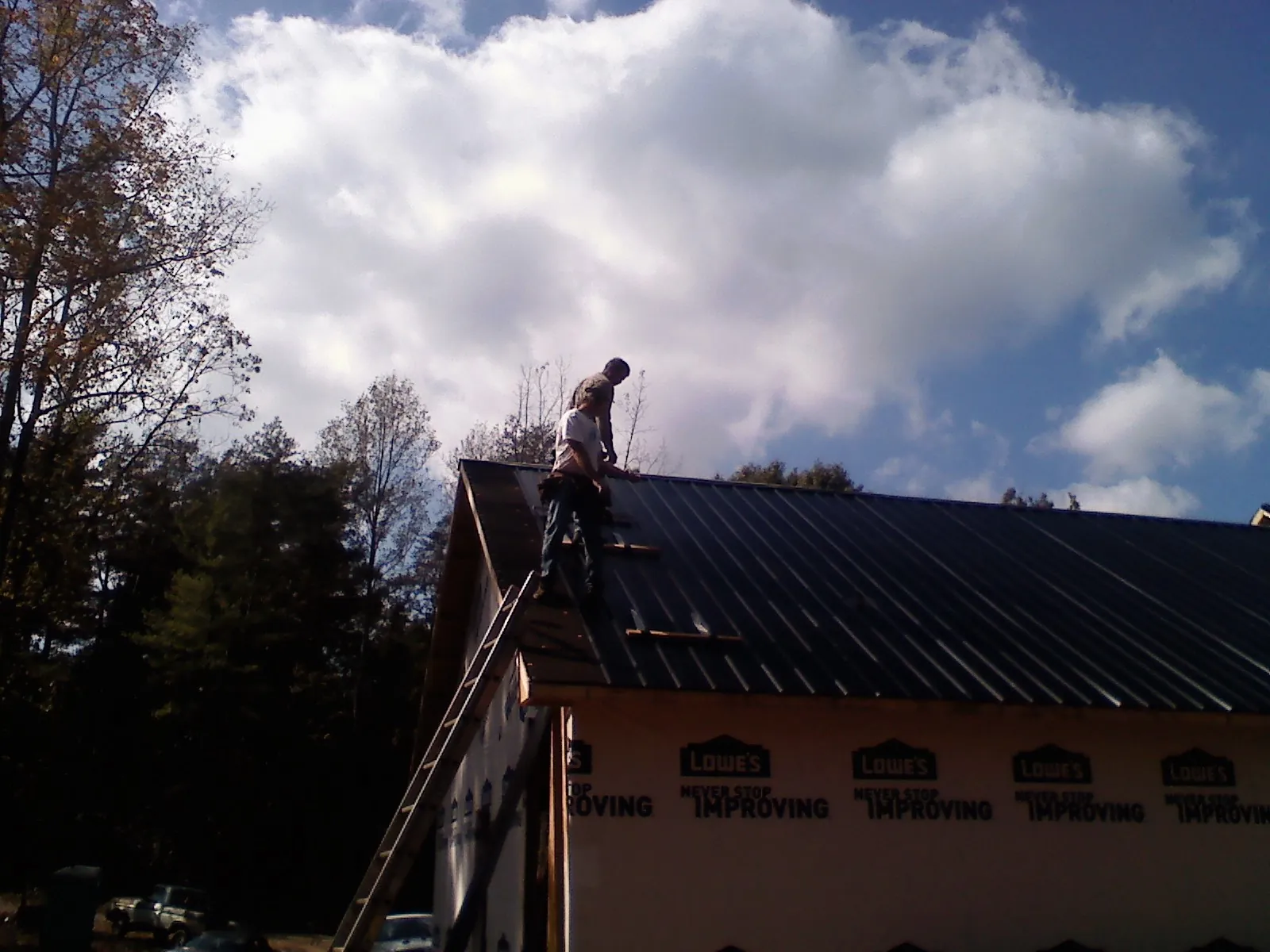 Roofer fastening dark metal panels high against a cloudy sky, from a Roof Inspection job in Harpersville