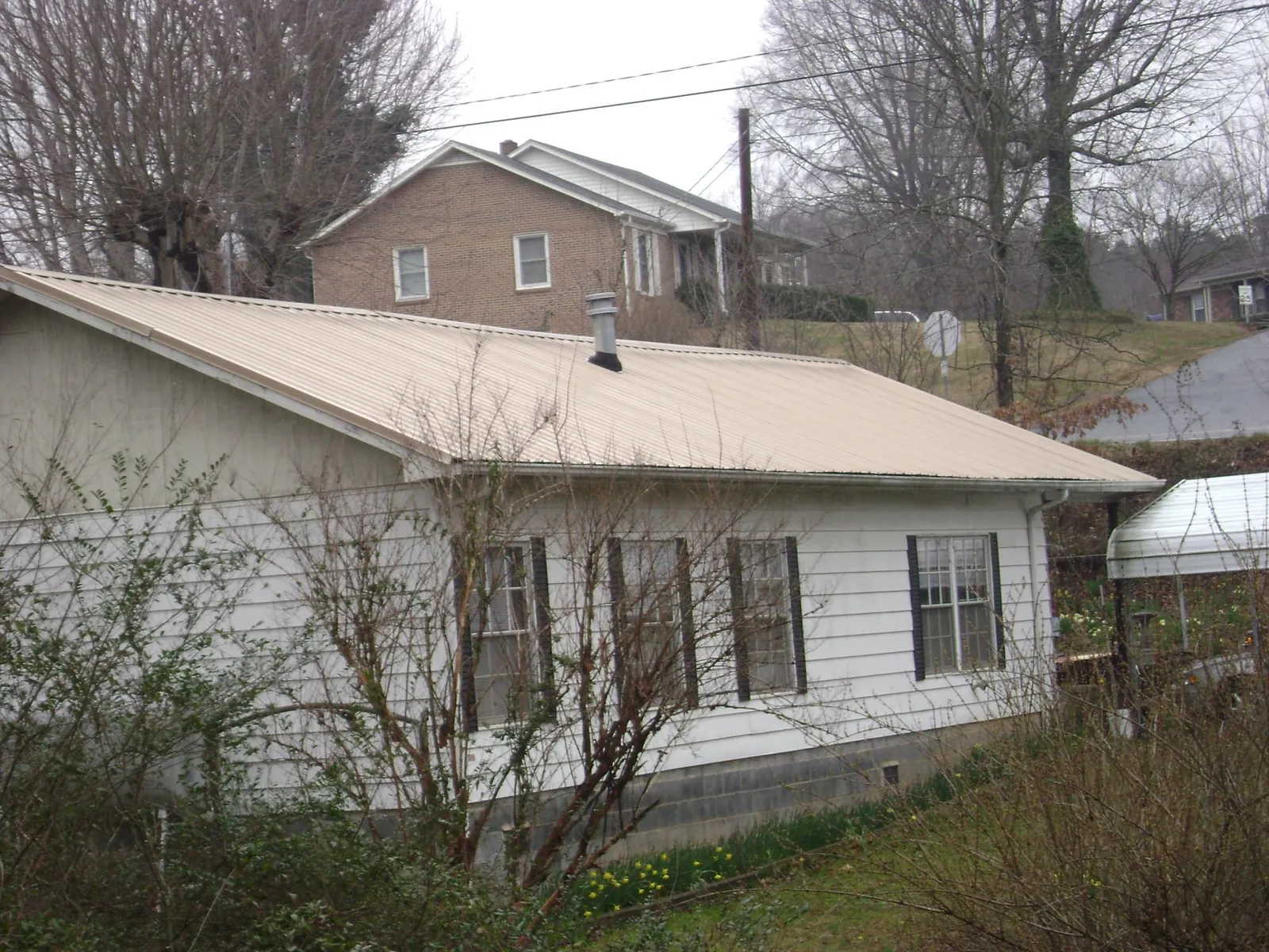 Tan metal roof on a white sided house set into a hillside — Commercial Roofing by Roofing Brothers in Harpersville