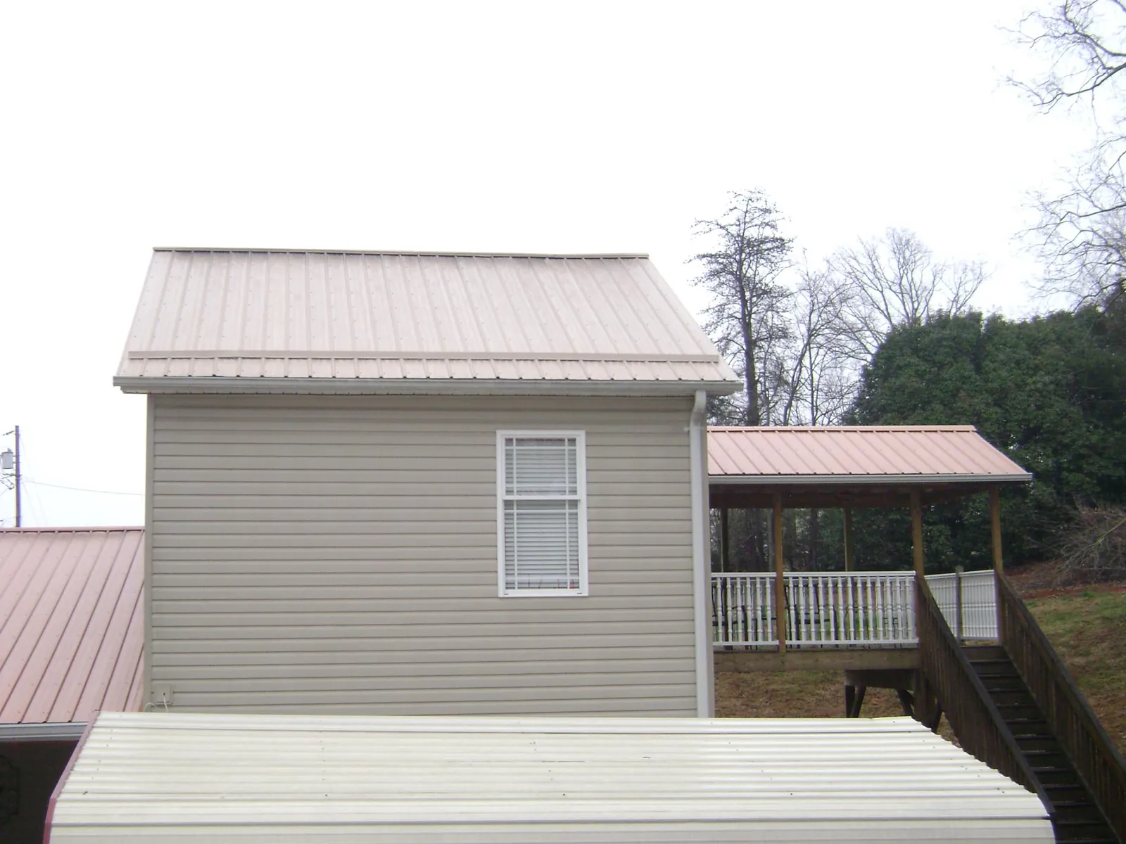 Tan metal roofs on a two story addition and attached porch, from a Roof Replacement job in Harpersville